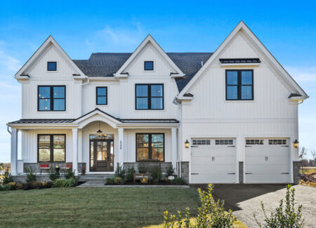 Stunning two-story modern farmhouse with a white exterior, black-trimmed windows, and a neatly landscaped front yard. The home features a covered front porch, double garage, and a charming gable roof, all set against a bright blue sky.