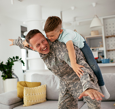 man in uniform with a kid on his back playing airplane